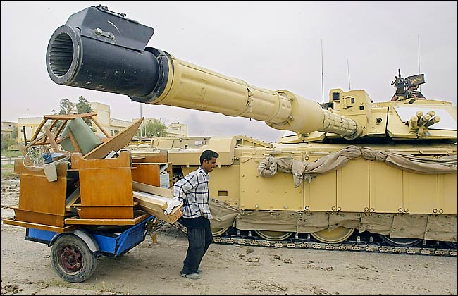 A local man drags his booty under the barrel of a British Challenger tank, Basra, April 7, 2003.